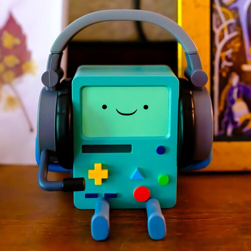 BMO from Adventure Time. A vinyl figurine of BMO sitting on a wooden mantle in front of framed images that are out of focus